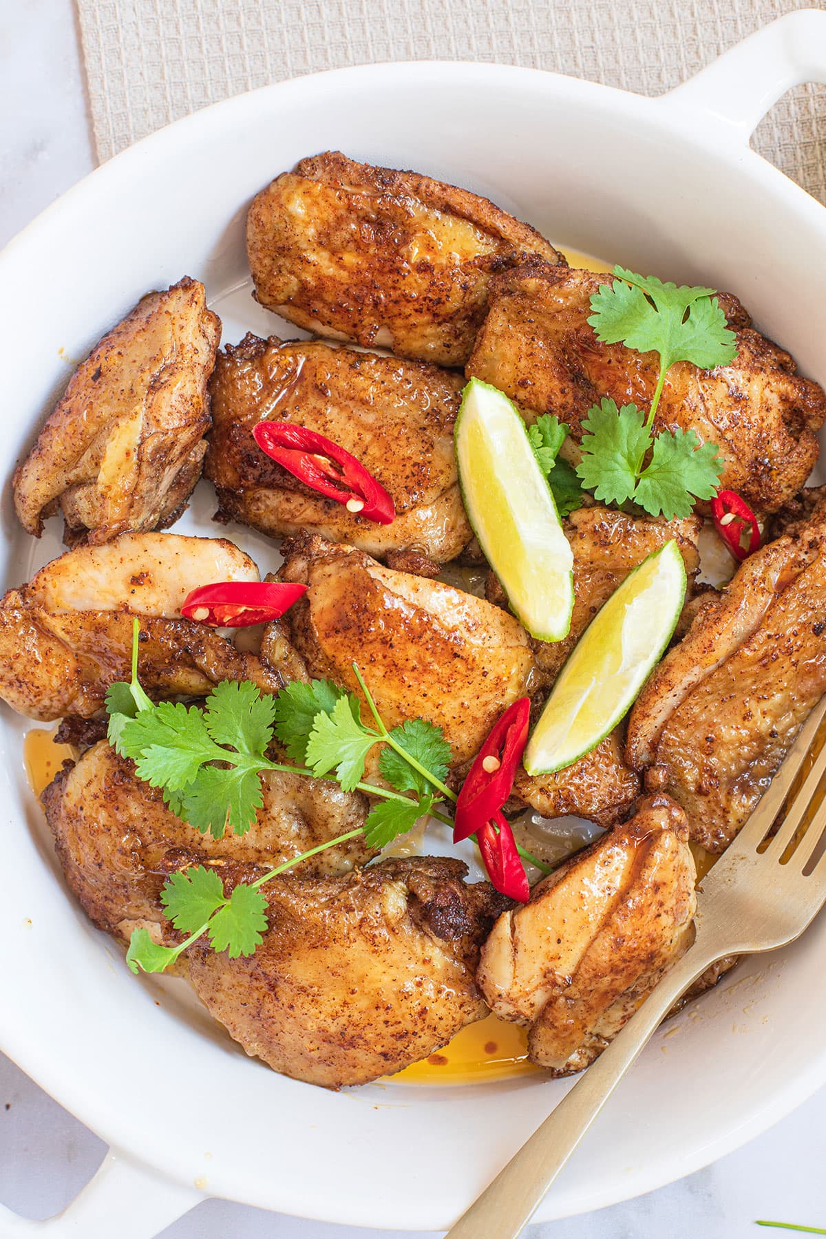 Golden-brown glazed chicken with a flavorful blend of spices served in a plate with fork on the side. 