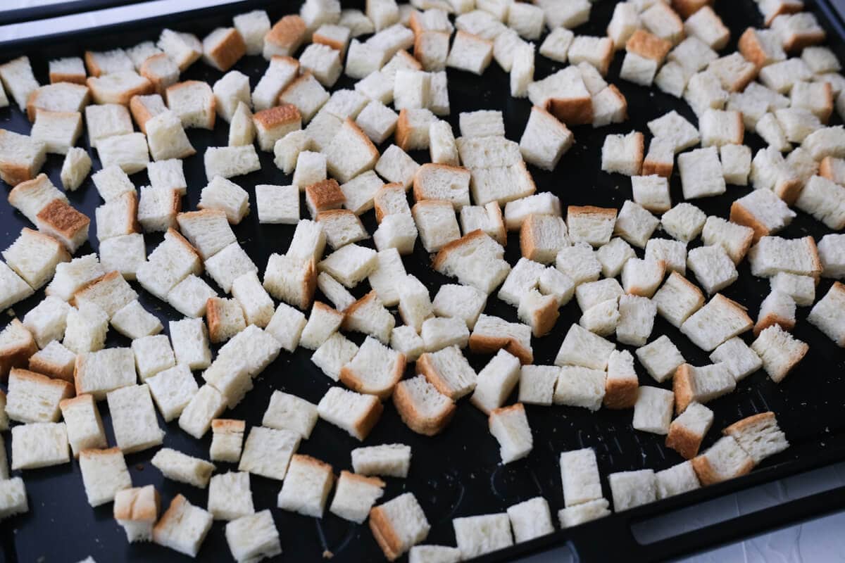 Small pieces of cubed white bread arranged on a oven tray. 