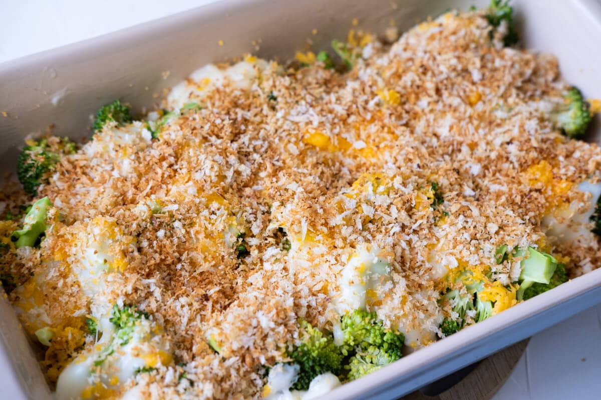 Broccoli arranged perfectly layered with creamy sauce, grated sharp cheddar cheese, and bread crumbs on top in a baking dish. 