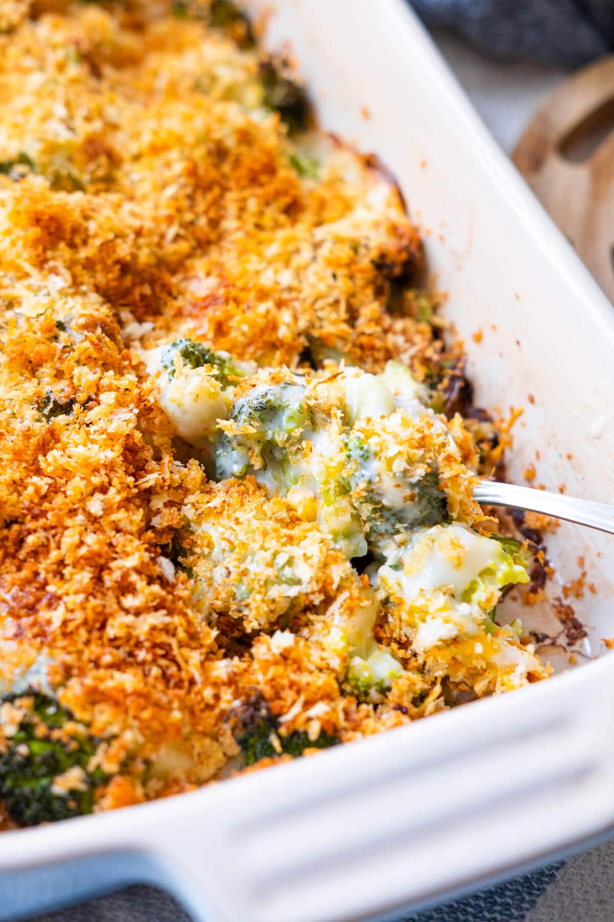 Close up shot of freshly baked broccoli gratin with broccoli covered in creamy sauce and topped with golden brown bread crumbs scooped by a spoon. 