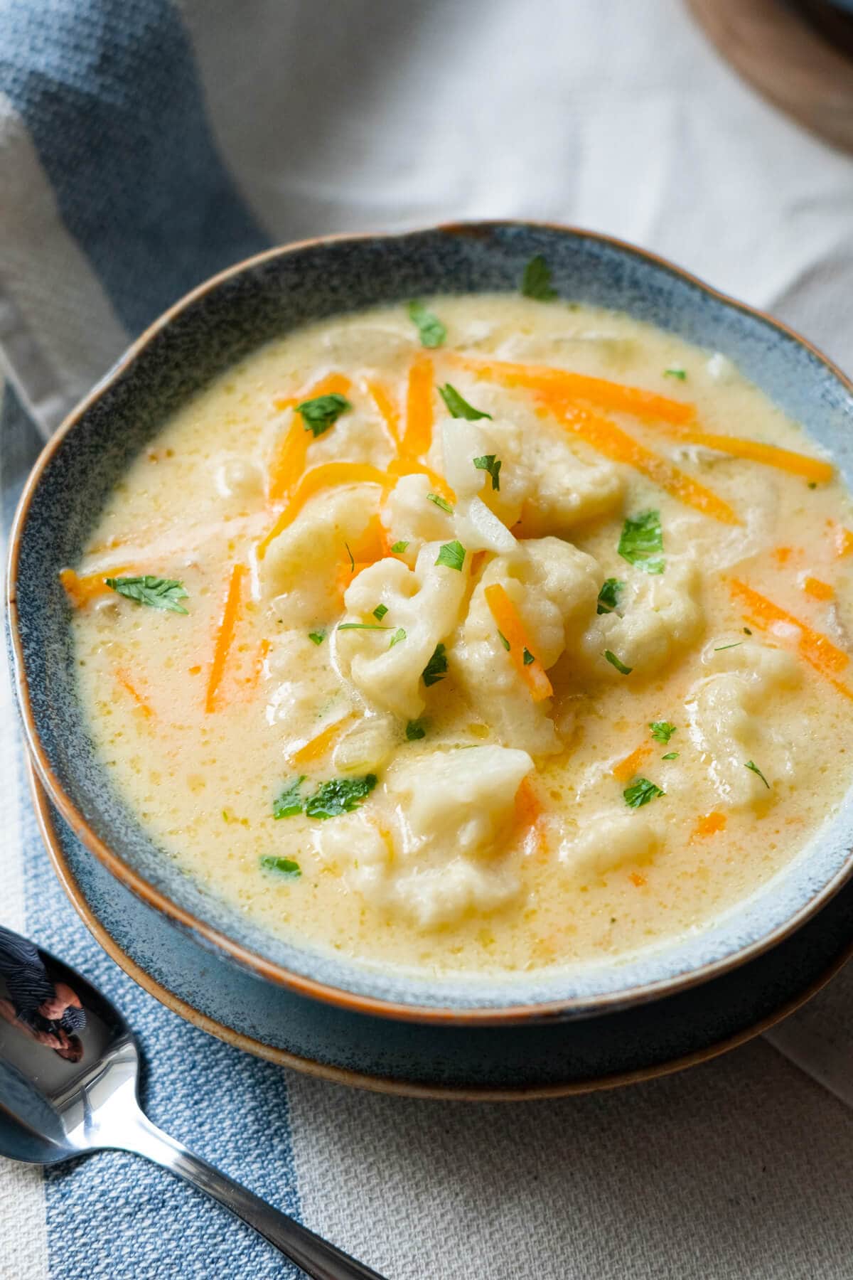 Creamy cauliflower soup served with chopped parsley and carrot shreds in a blue bowl. 