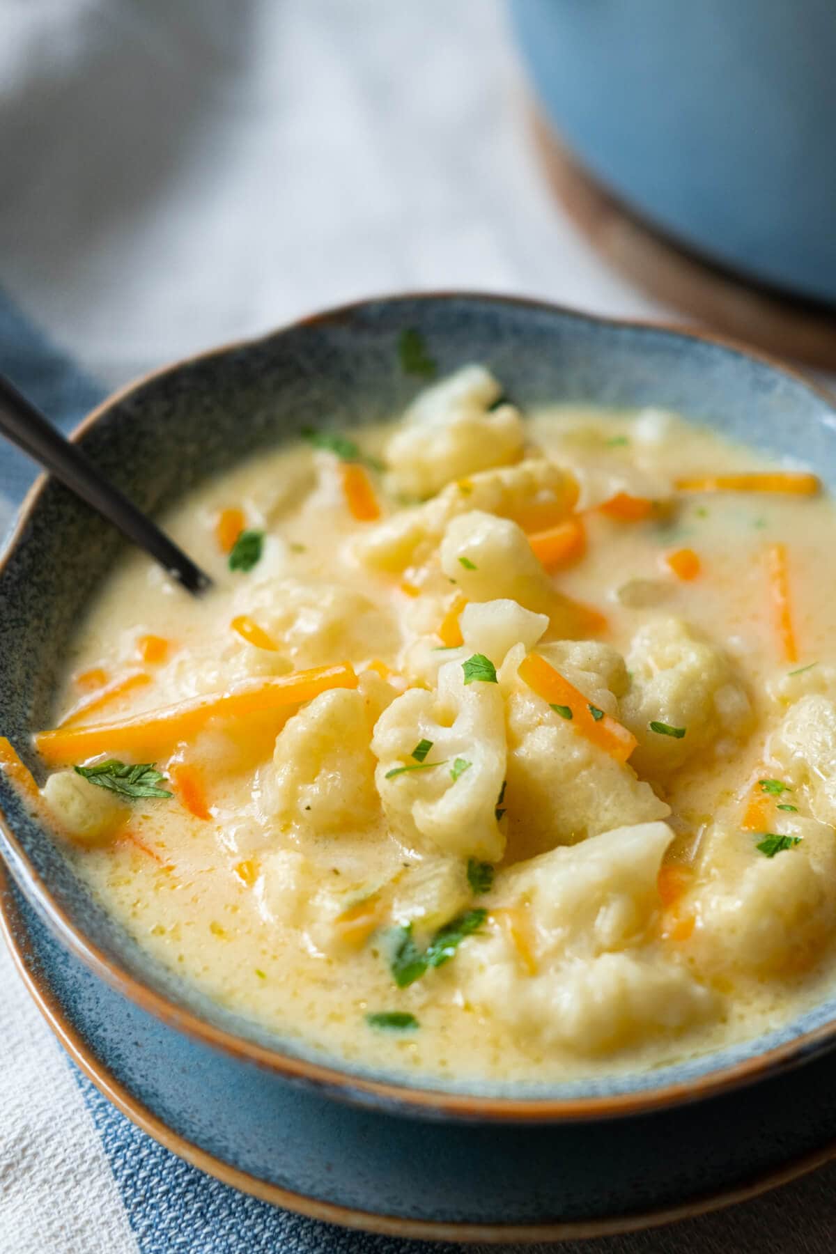 Overloaded tender white cauliflower with shreds of carrots and sprinkled parsley in a cheesy soup base served in a bowl.