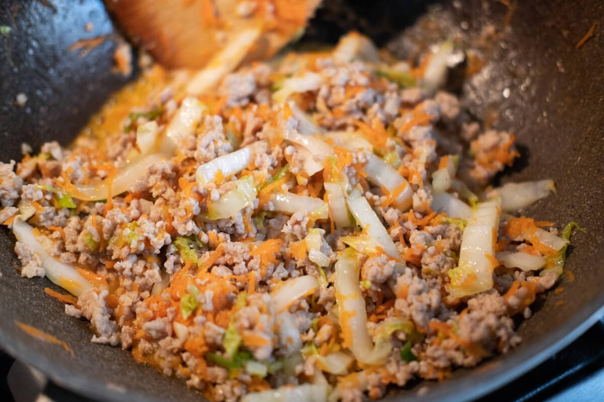 Ground chicken stir fried with shredded cabbage, shredded carrots, and sliced  green onions in a wok. 