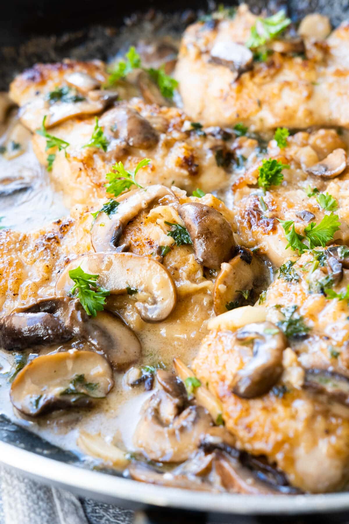 Close up shot of golden-brown chicken thighs and mushrooms coated in flavorful Marsala wine sauce in a skillet.