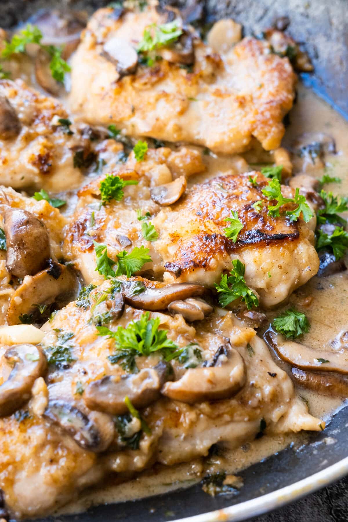 Appetizing chicken thigh pieces bathed in rich Marsala sauce beautifully presented in a black plate.