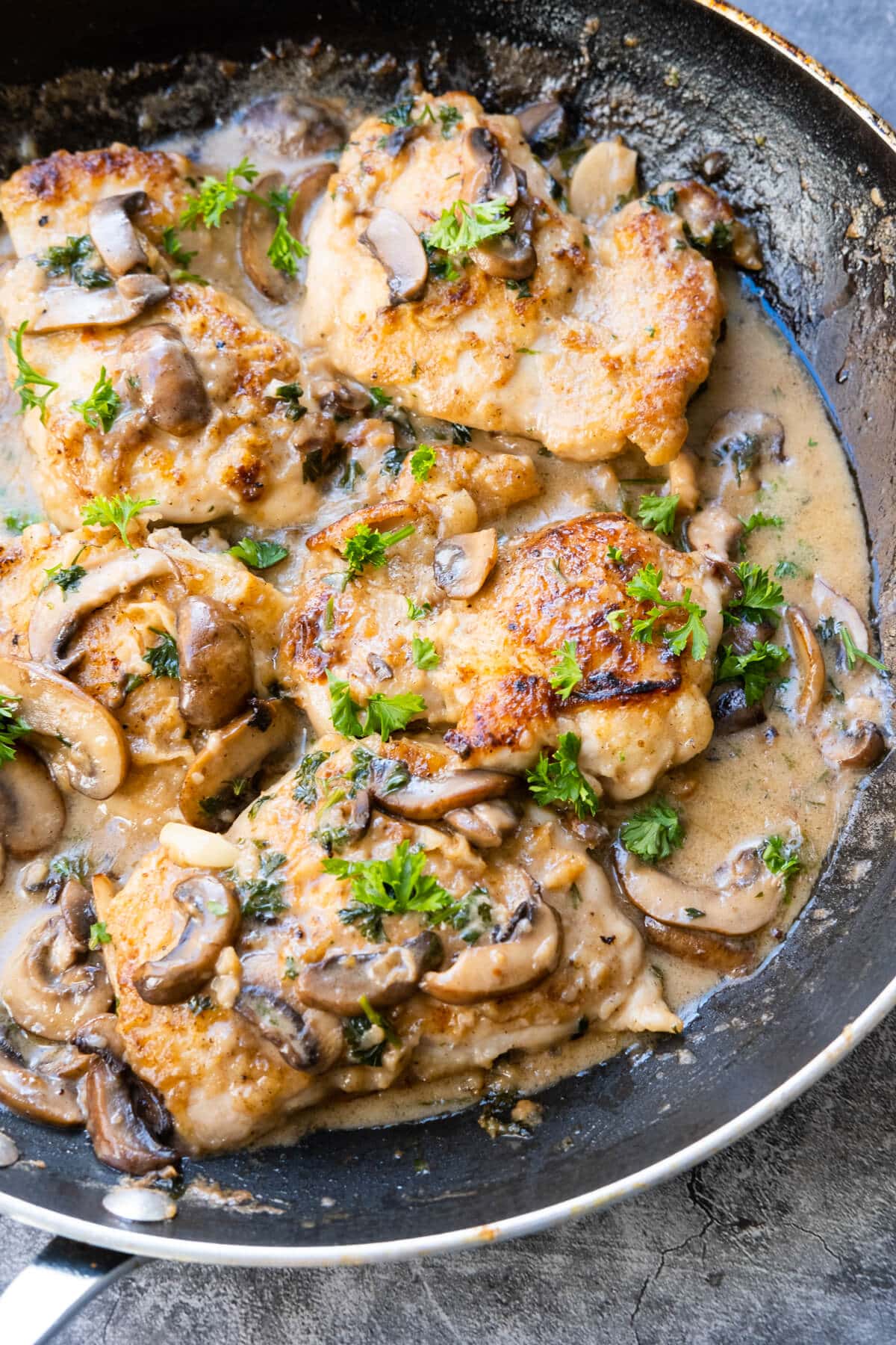 Golden-brown seared chicken pieces and mushrooms soaked in flavorful Marsala wine sauce in a skillet. 