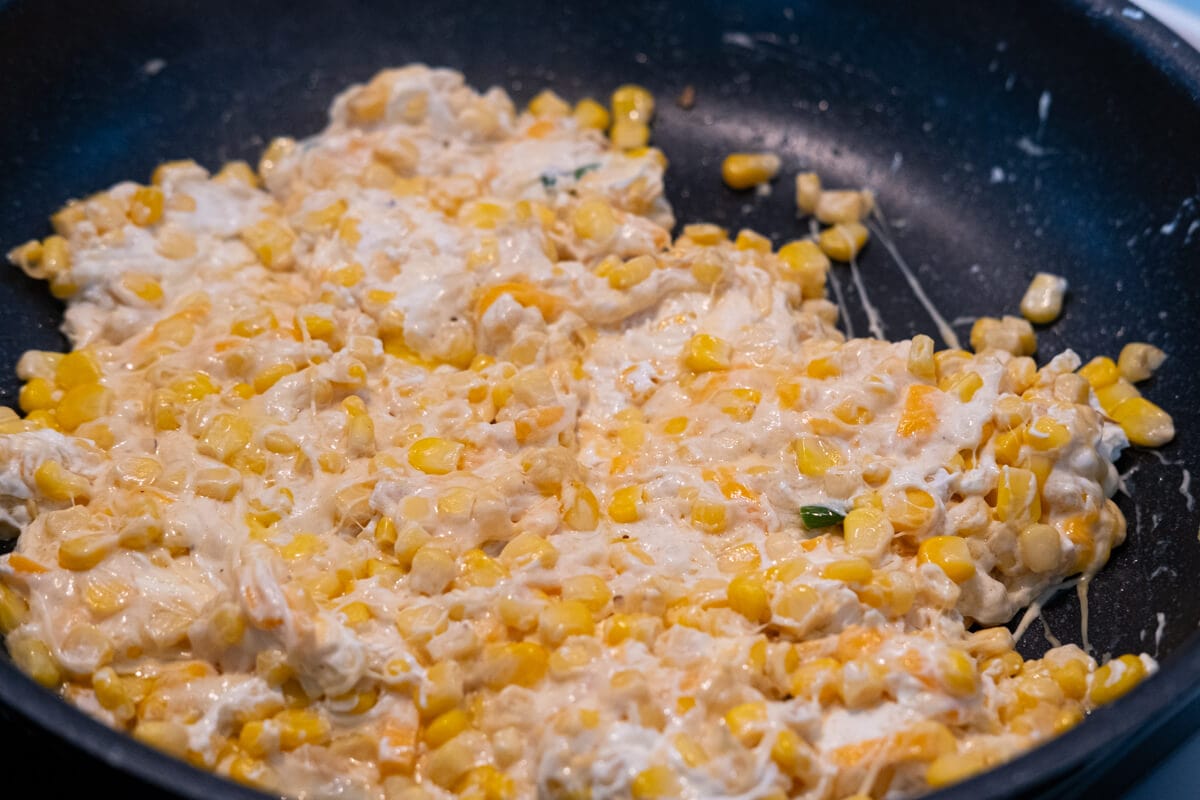 Corn, cream cheese, shredded mozzarella cheese, and cheddar cheese combined with melted butter, green chili pepper, and garlic in a skillet.  