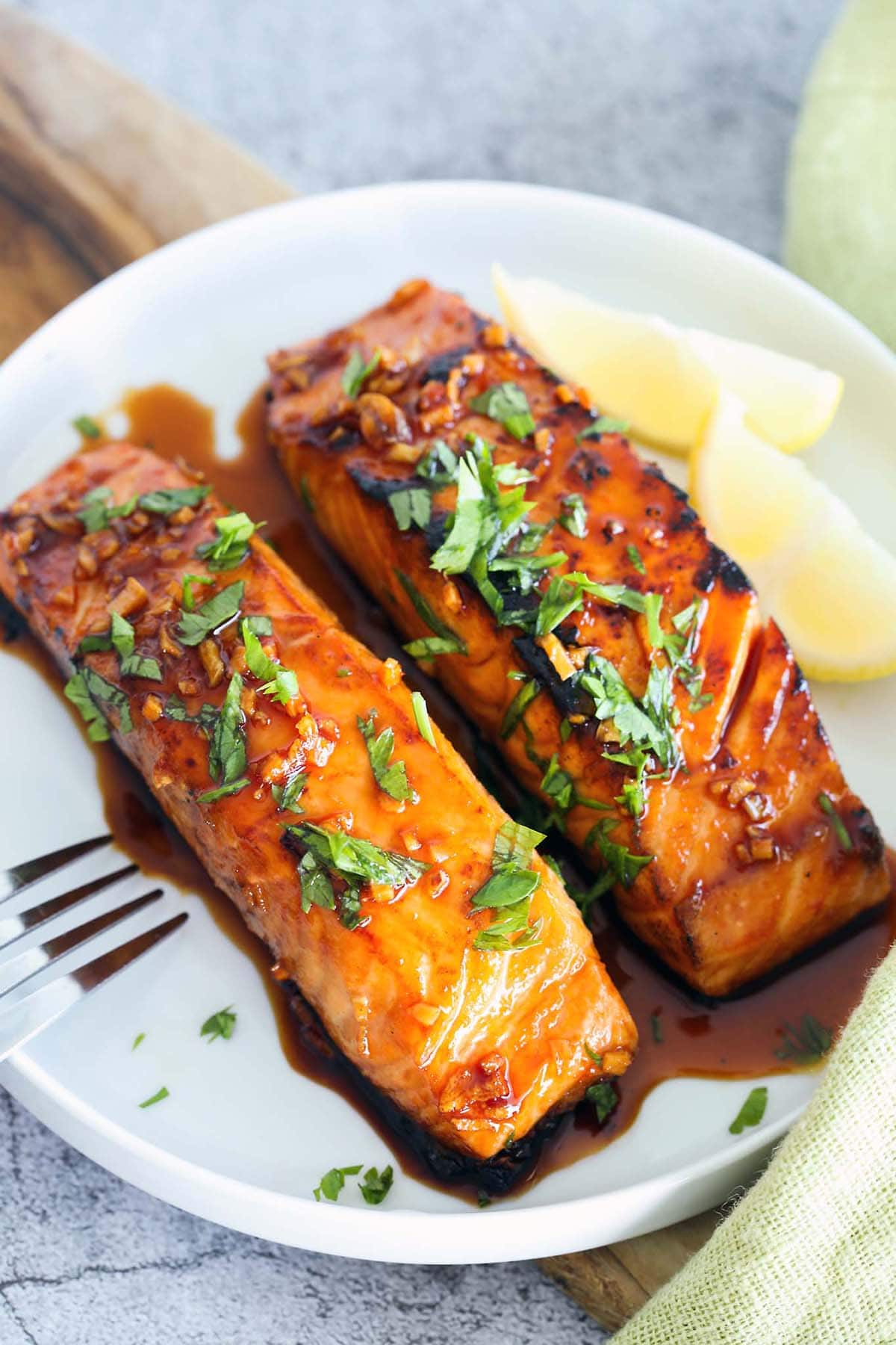 A piece of salmon glazed with honey sriracha served on a plate with lemon wedges on the side.