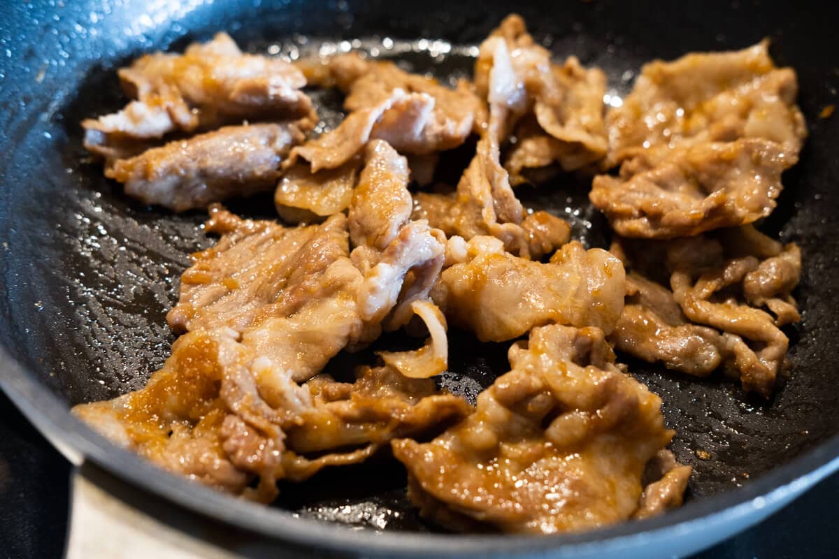 Pork slices being stirred fried with ginger sauce in a pan. 