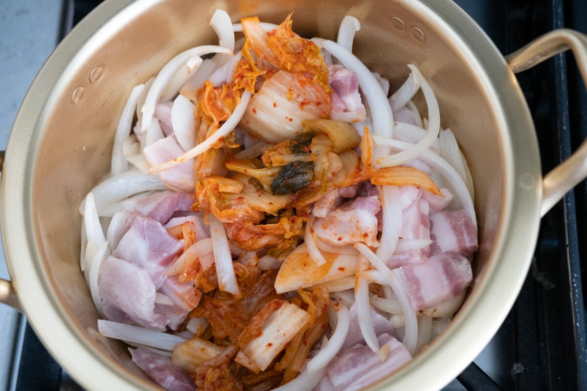 Sliced onion, kimchi and pork belly in the pot. 