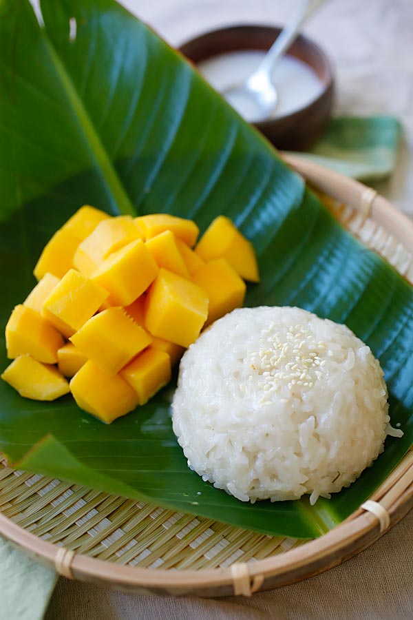 Mango sticky rice with coconut milk and fresh mangoes served on banana leaves.