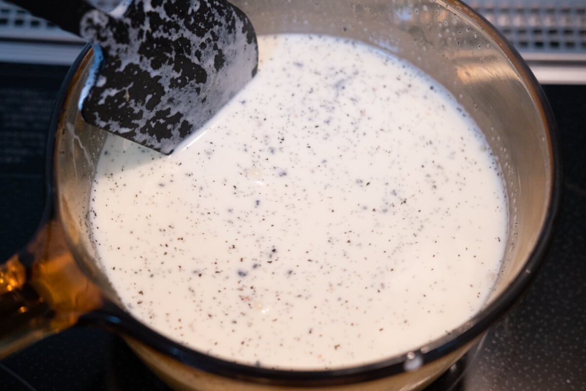 A mixuture of hevay cream, milk, vanilla seed, and sugar boiling in a saucepan. 