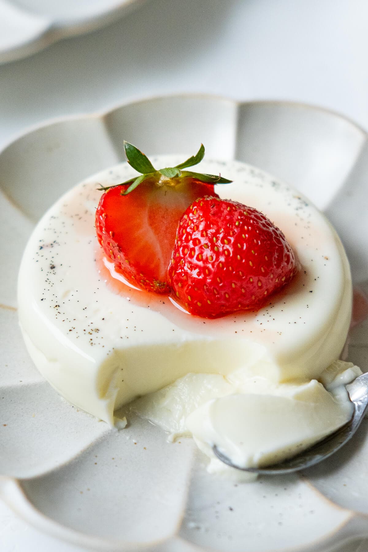Silky, smooth panna cotta with strawberry on top served on a plate. 