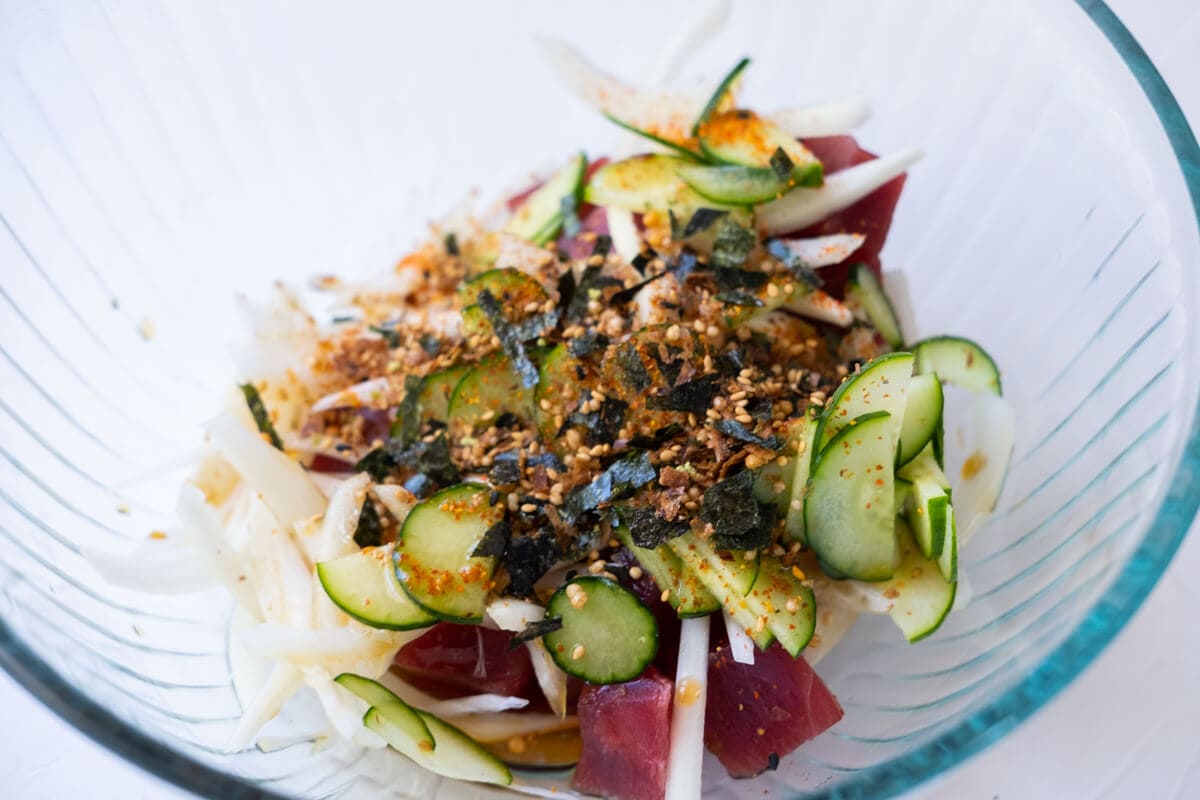 Bite-sized fresh tuna, thinly sliced yellow onion, thinly sliced cucumber, furikake, and Japanese chili pepper mixed in a bowl. 