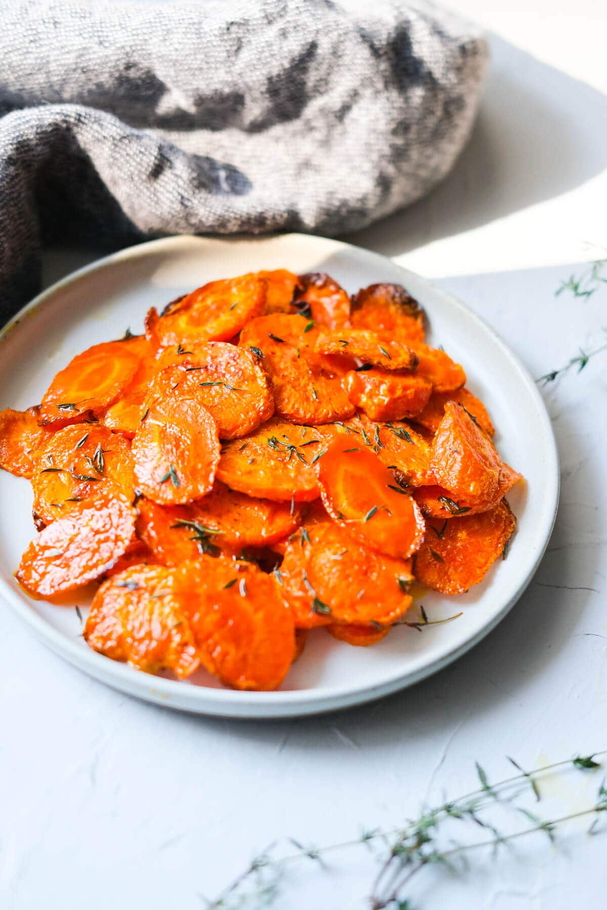 Cooked carrots in a plate with a kitchen towel and fresh thyme on the side. 