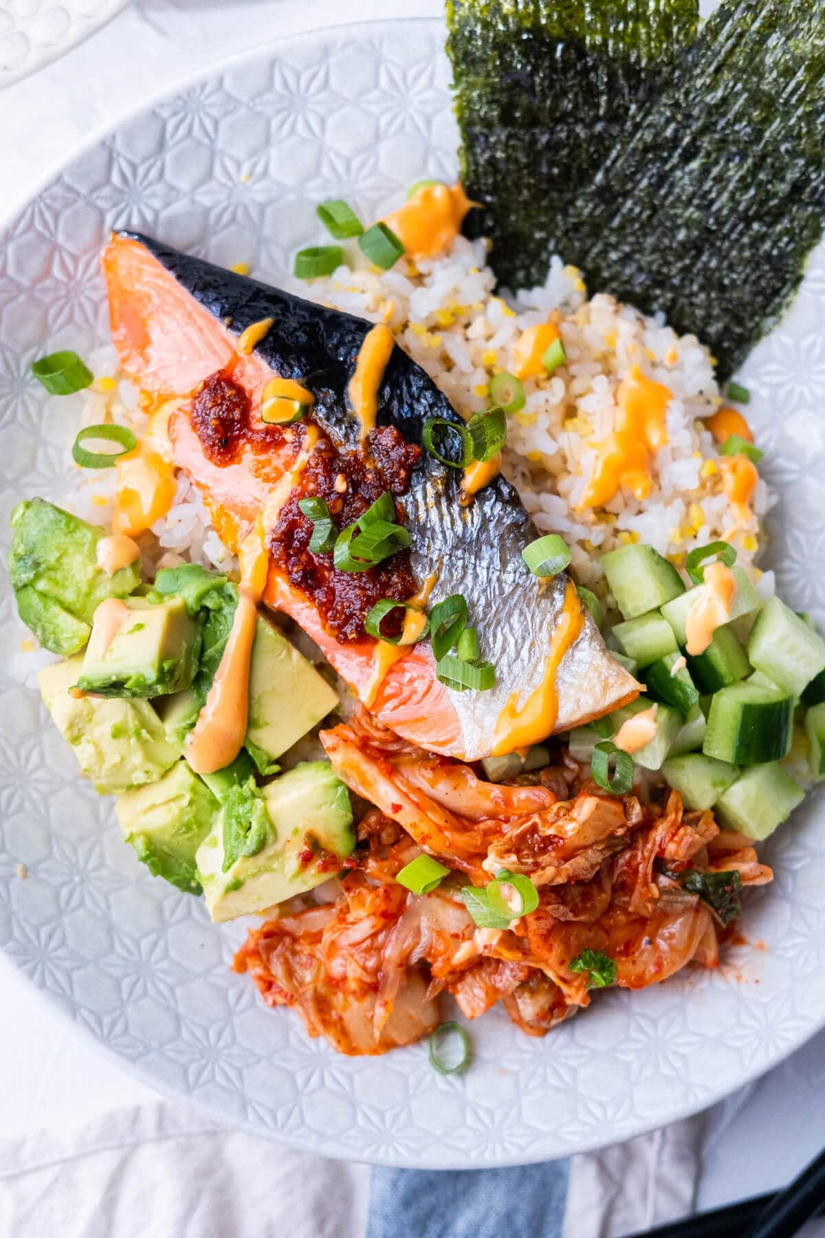Baked salmon, avocado, cucumber and kimchi over brown rice, garnish with green onion and spicy tamari sauce. 