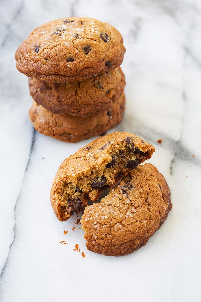 A stack of chocolate chip cookies topped with flaky sea salts and loaded with chocolate chips.