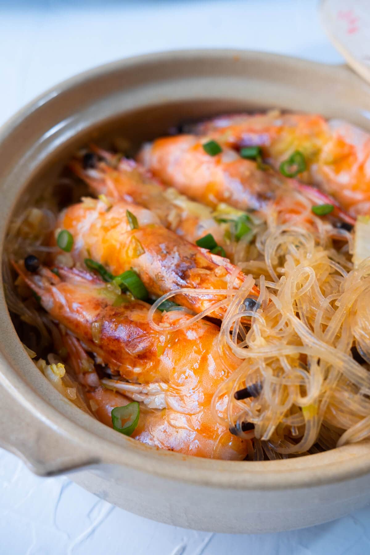 Glass noodles and prawns served in a clay pot with chopped green onion sprinkled on top. 