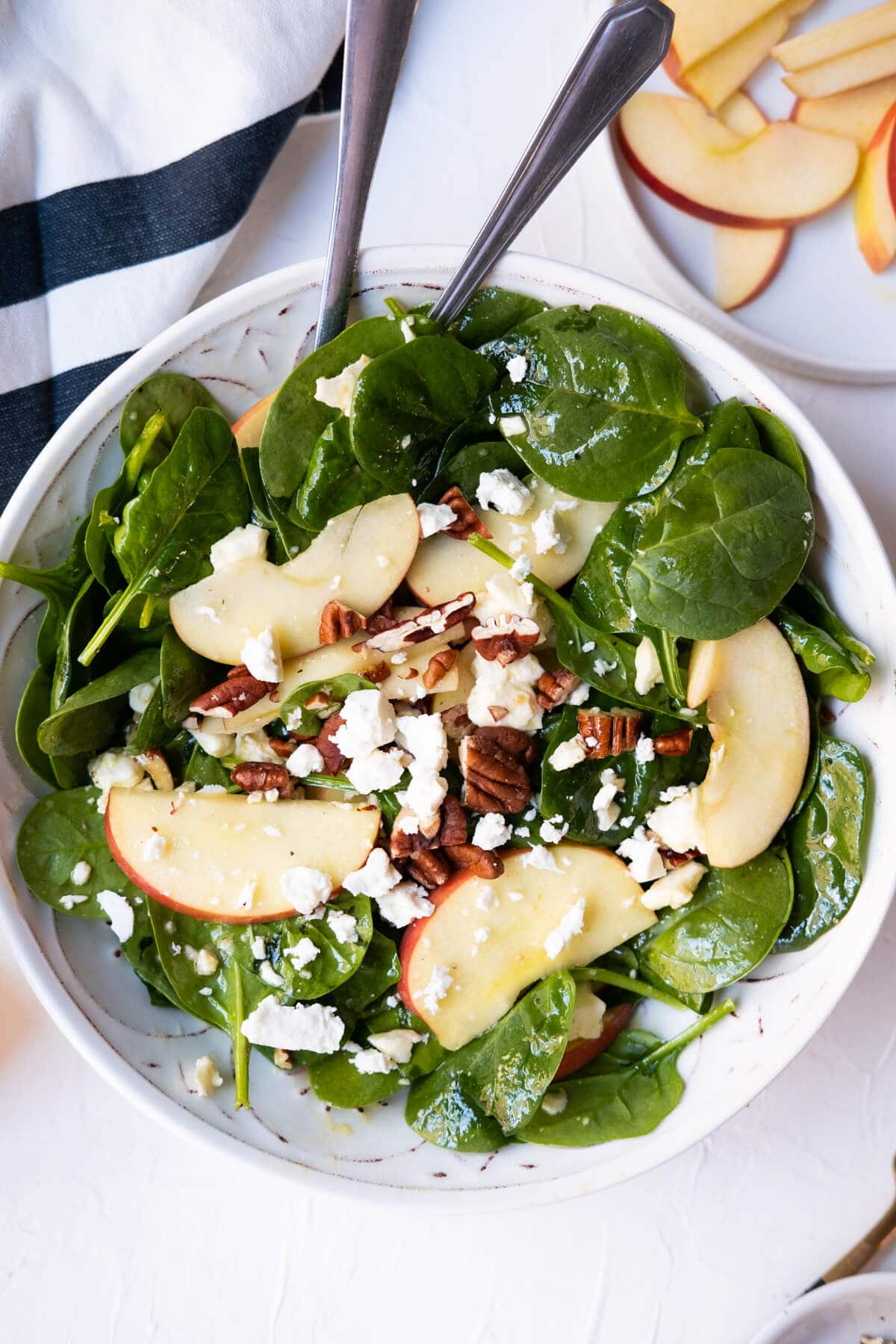Spinach with apples, pecans and feta in a bowl and served with extra apple slices aside. 