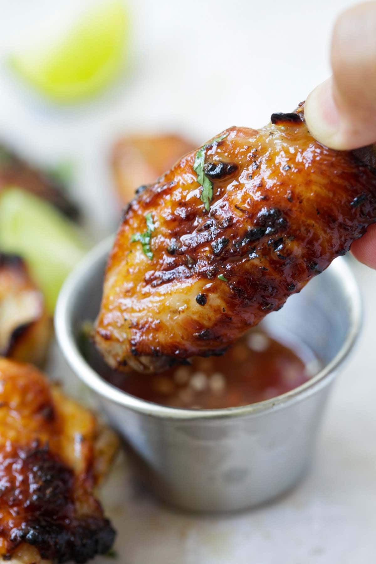 Grilled chicken wings with brown glaze dipped in Thai sauce.